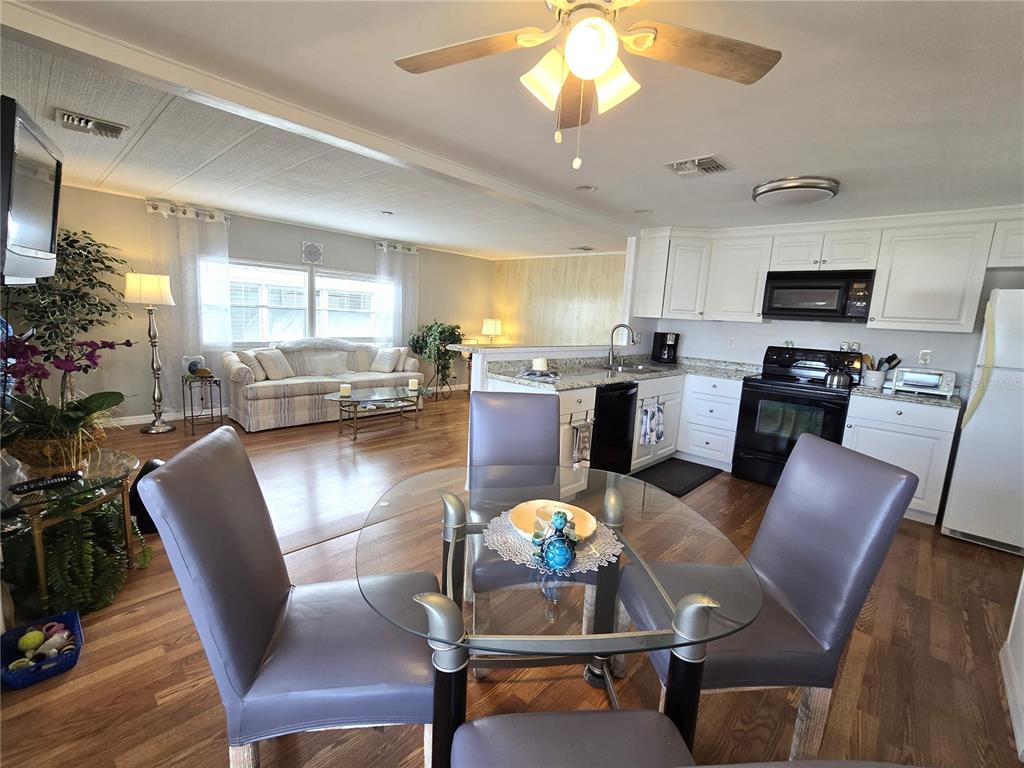 An open-concept kitchen and living area features white cabinets, a glass dining table, and wood flooring — 2122 WATERVIEW DRIVE, HOLIDAY, FL