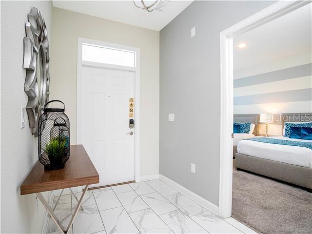 An entryway with a white door, marble-look tile flooring, and a view into a bedroom — 1568 MAIDSTONE COURT, DAVENPORT, FL