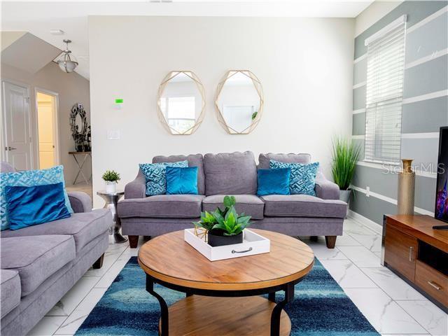 A living room features a gray sofa, a round wooden coffee table, and two wall mirrors — 1568 MAIDSTONE COURT, DAVENPORT, FL