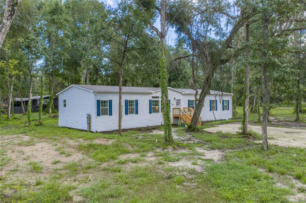 A white manufactured home with blue shutters sits on a wooded lot with grass — 11957 SW 35TH STREET, WEBSTER, FL