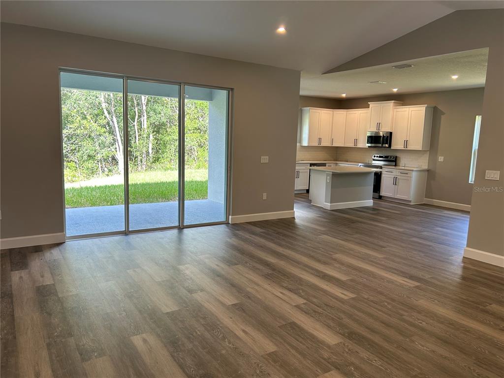 An open-concept living area features wood-look flooring, sliding glass doors, and a white kitchen — 8038 N VOYAGER DRIVE, DUNNELLON, FL