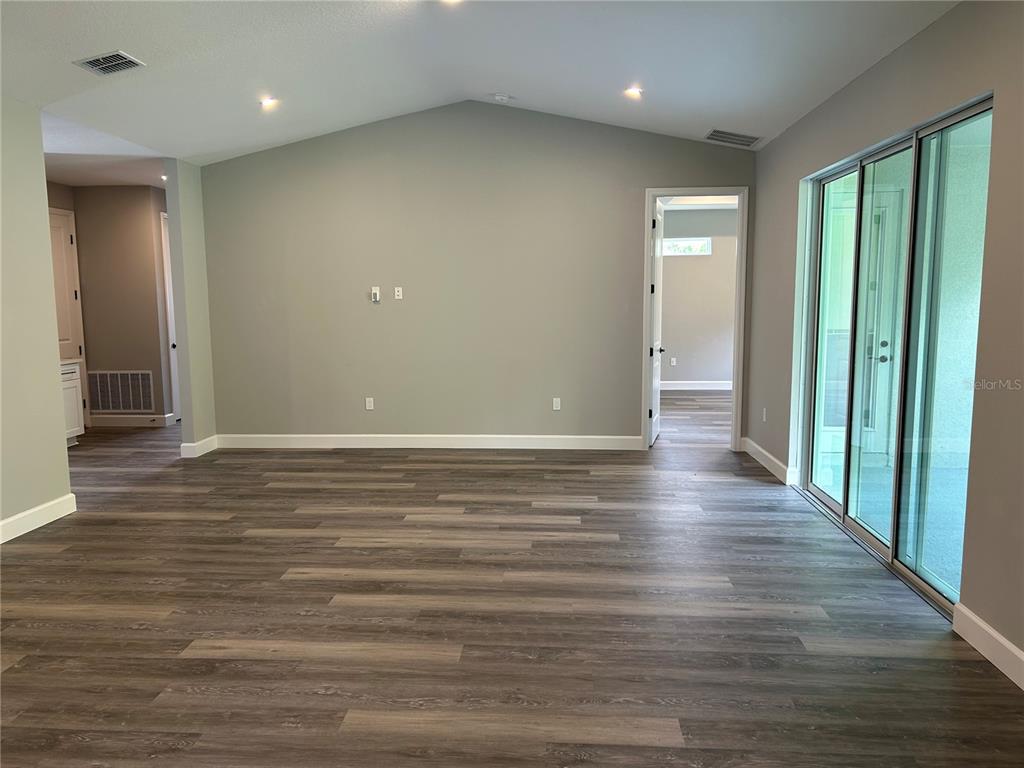 An empty room features gray walls, vaulted ceilings, wood-look flooring, and sliding glass doors — 8038 N VOYAGER DRIVE, DUNNELLON, FL