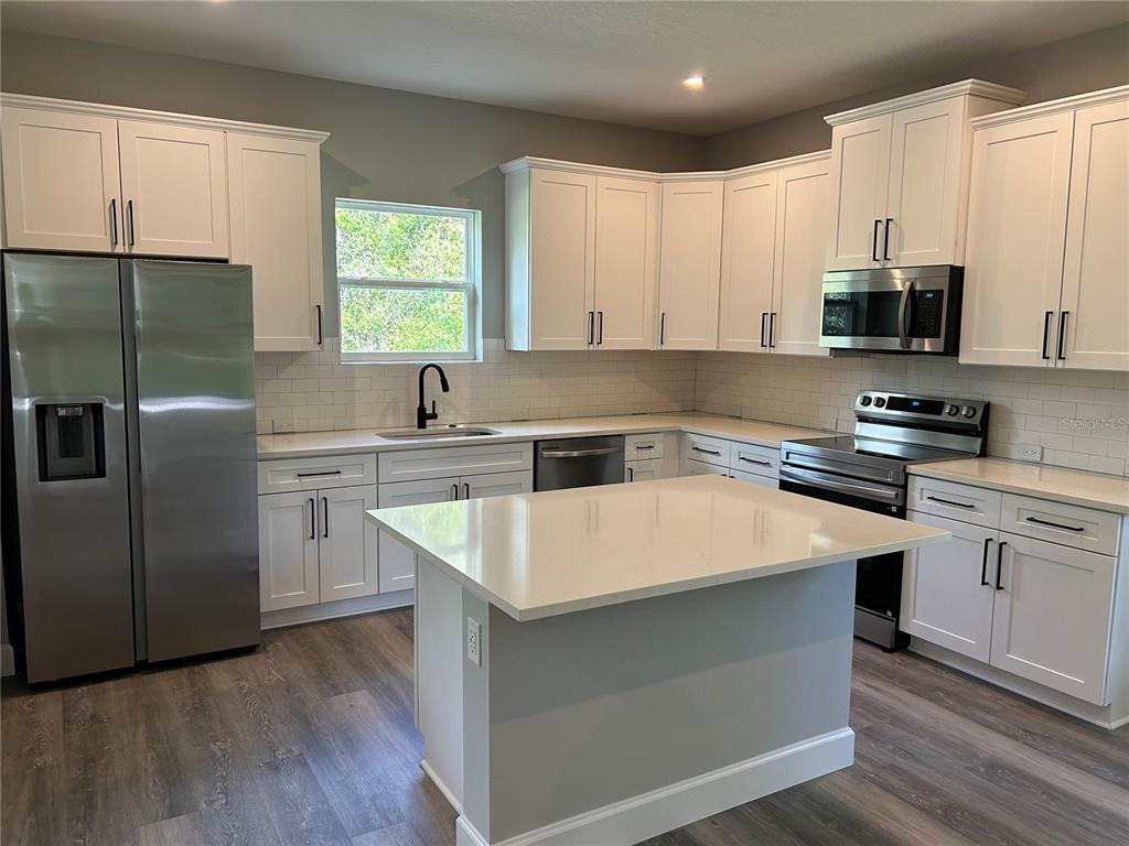 A kitchen features white cabinets, stainless steel appliances, a center island, and wood-look flooring — 8038 N VOYAGER DRIVE, DUNNELLON, FL