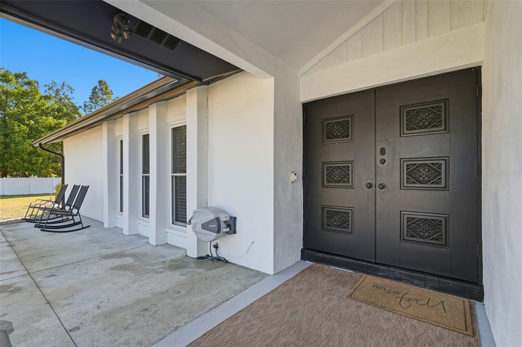 A covered concrete porch features a black double front door and two black rocking chairs — 6370 90TH AVENUE N, PINELLAS PARK, FL