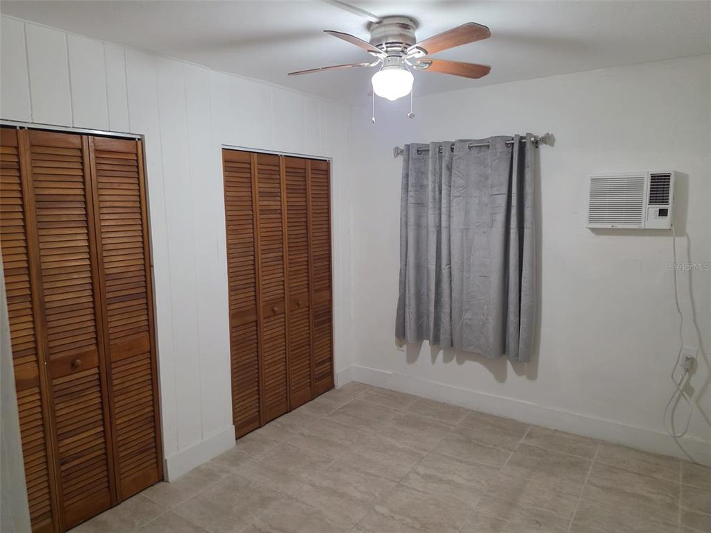 A bedroom features tile flooring, two wooden louvered closets, a ceiling fan, and a window unit — 1844 JOHN RIVERS STREET UNIT S, SARASOTA, FL