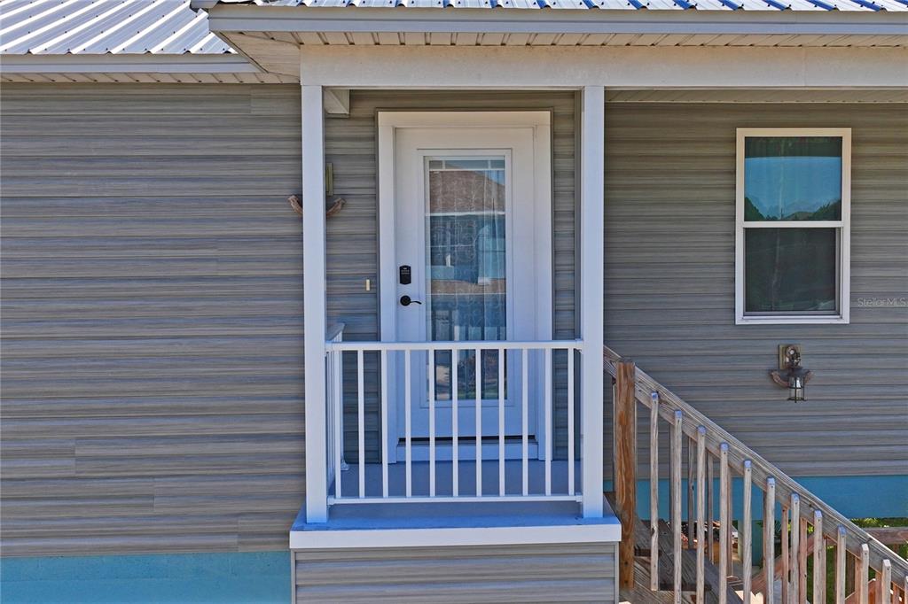 A white front door with a glass panel is centered on a grey-sided house exterior — 3270 HIBISCUS DRIVE, HERNANDO BEACH, FL
