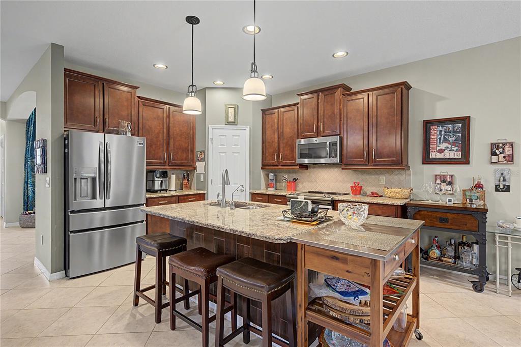 A kitchen features dark wood cabinets, granite countertops, a central island, and stainless steel appliances — 29358 GRASS BUNKER DRIVE, SAN ANTONIO, FL