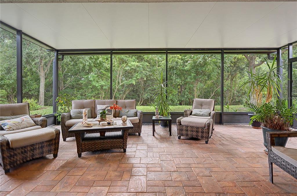 A screened-in patio with wicker furniture, a tile floor, and a view of dense trees — 29358 GRASS BUNKER DRIVE, SAN ANTONIO, FL