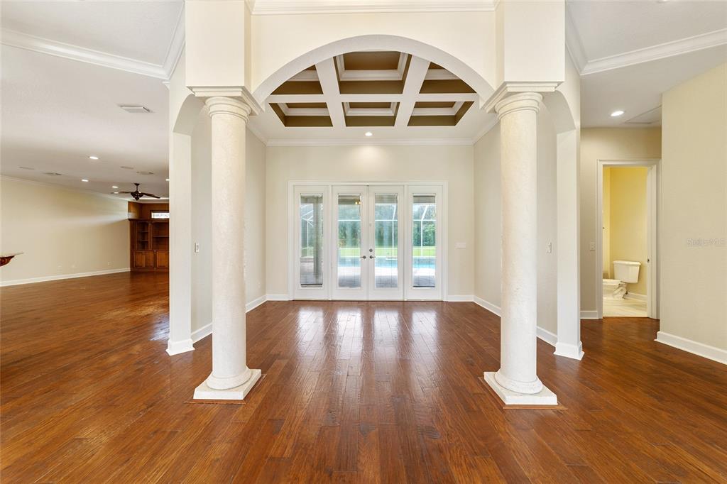 A spacious room with hardwood floors, two white columns, and a coffered ceiling archway — 8280 SE 15TH COURT, OCALA, FL