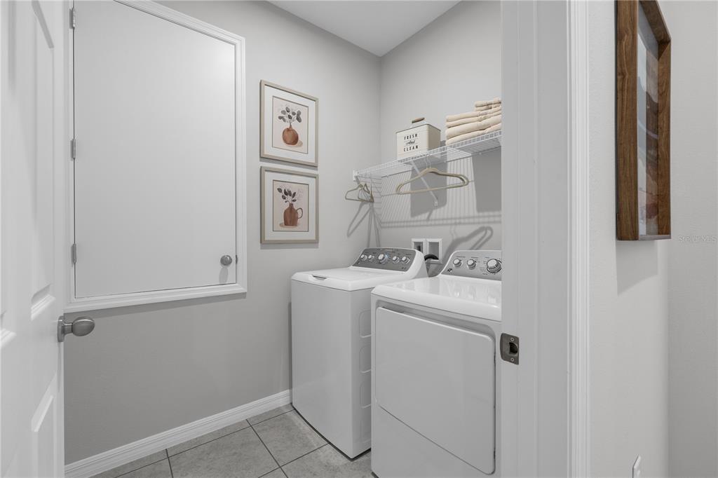 A laundry room features a white washer and dryer, wire shelving, and two framed wall prints — 1413 CHAMBORD DRIVE, EAGLE LAKE, FL