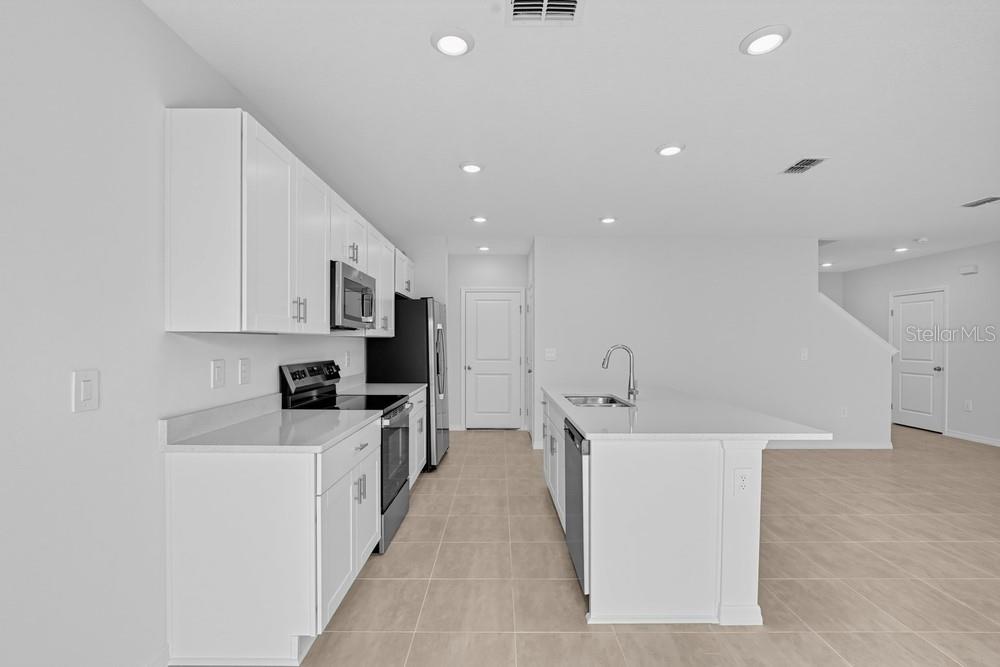 A kitchen with white cabinets, granite countertops, and a central island overlooking a living area — 12422 WHISK COURT, HUDSON, FL