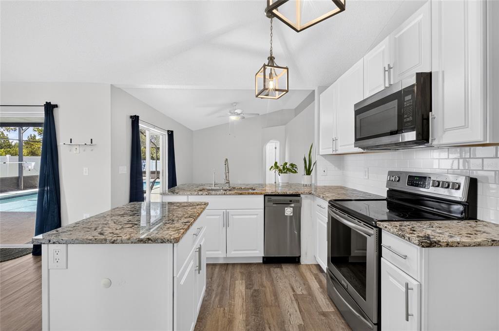 An open living area features gray wood-look flooring, vaulted ceilings, and sliding doors to a pool — 718 TOULON DRIVE, KISSIMMEE, FL