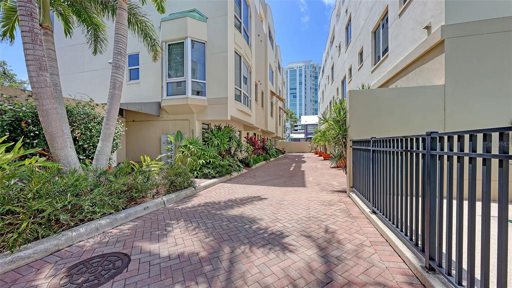 A paved walkway runs between two multi-story buildings with palm trees and landscaping — 235 COCOANUT AVENUE UNIT 128E, SARASOTA, FL