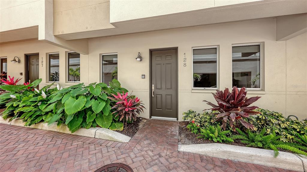 A brown front door is flanked by windows and landscaping on a brick-paved walkway — 235 COCOANUT AVENUE UNIT 128E, SARASOTA, FL