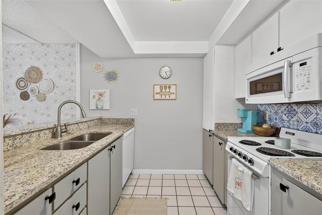 A kitchen with white cabinets, granite countertops, and a breakfast bar overlooking the space — 2614 COVE CAY DRIVE UNIT 405, CLEARWATER, FL