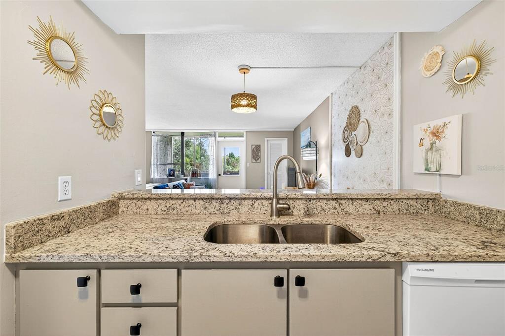 A kitchen features granite countertops, white cabinets, a stainless steel sink, and a tiled floor — 2614 COVE CAY DRIVE UNIT 405, CLEARWATER, FL