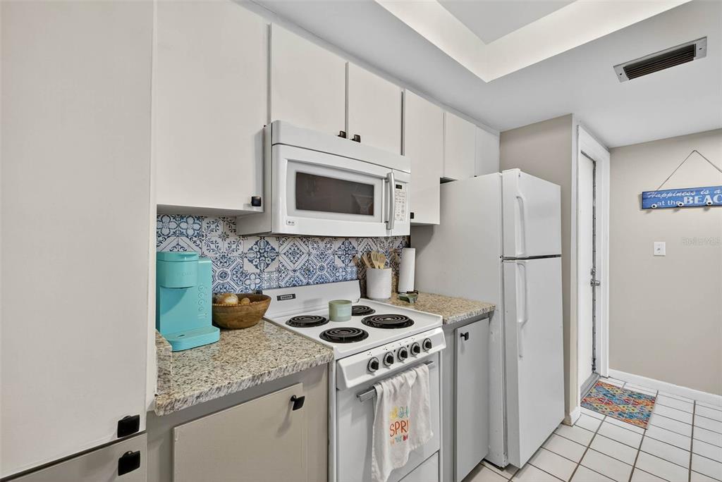 A kitchen sink with granite countertops overlooks a living area with decorative wall mirrors — 2614 COVE CAY DRIVE UNIT 405, CLEARWATER, FL