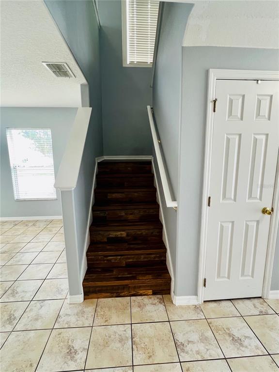 A staircase with dark wood treads leads upward between light blue walls and a white door — 13672 CYGNUS DRIVE, ORLANDO, FL