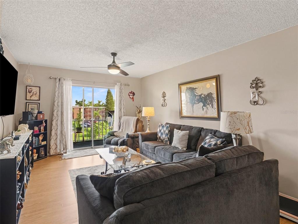 A living room features a dark sectional sofa, a glass coffee table, and a sliding door — 4171 HERON WAY UNIT E309, BRADENTON, FL