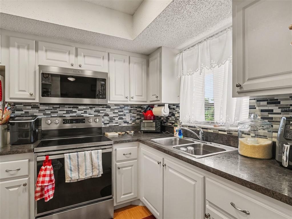 A kitchen with white cabinets, stainless steel appliances, a dark countertop, and a tiled backsplash — 4171 HERON WAY UNIT E309, BRADENTON, FL
