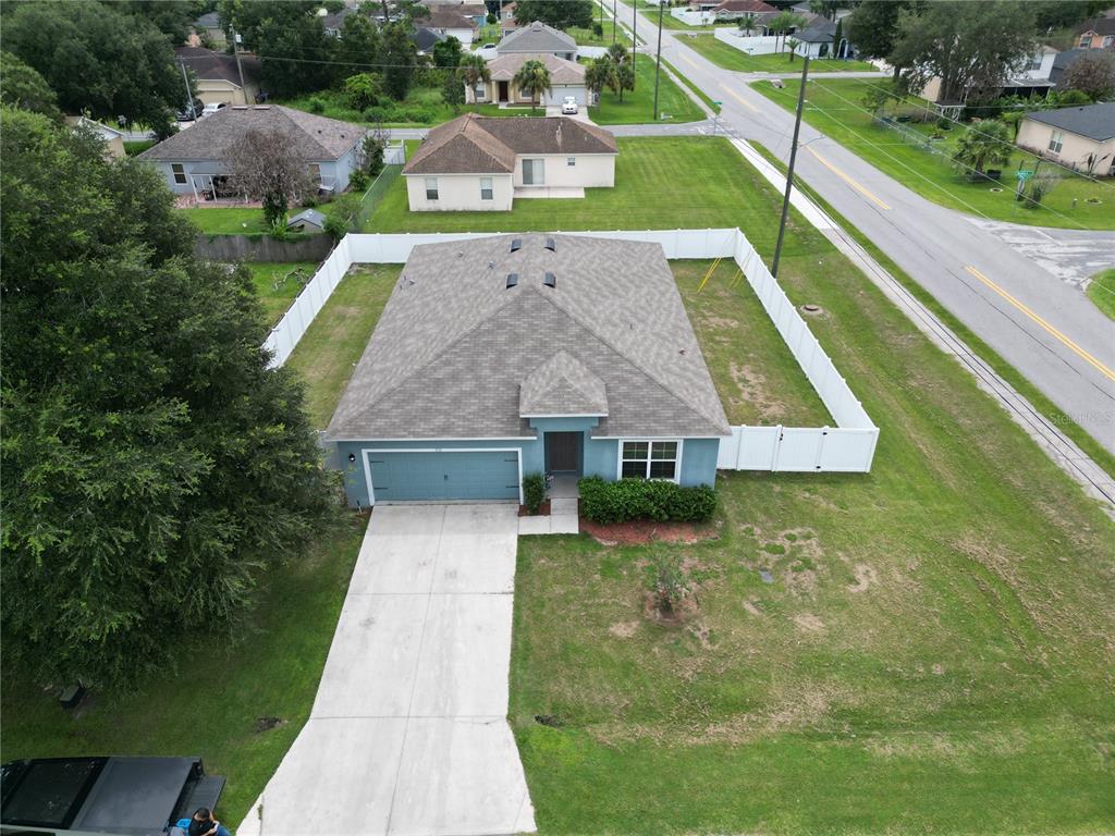 An aerial view shows a blue single-story house with a white fence and concrete driveway — 233 TIFFANY COURT, KISSIMMEE, FL