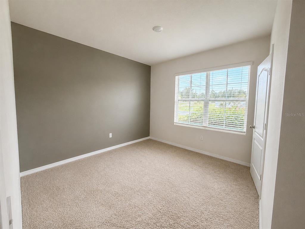 An empty bedroom features beige carpet, a grey accent wall, and a white window — 233 TIFFANY COURT, KISSIMMEE, FL