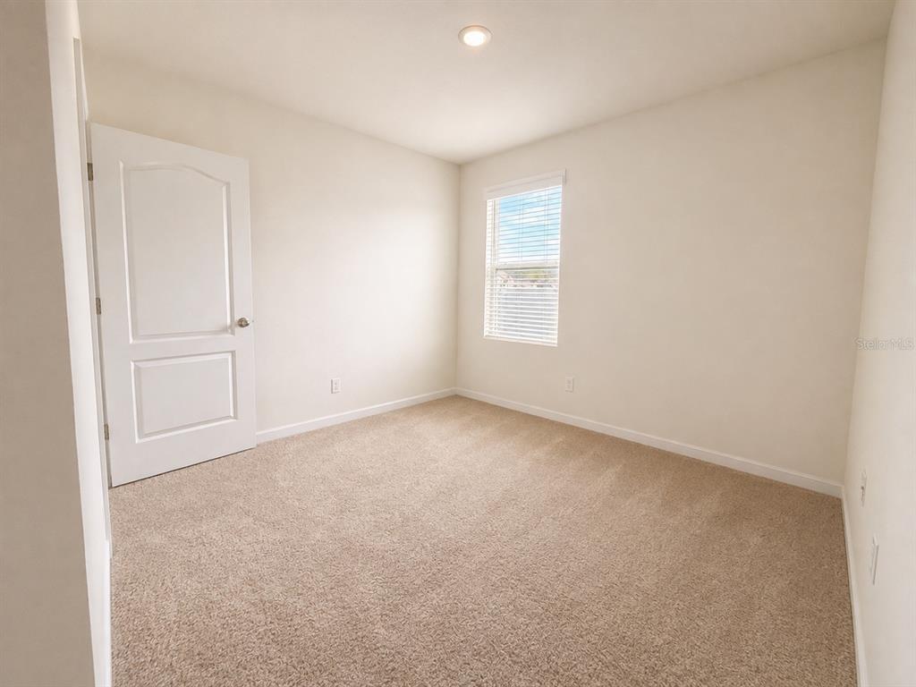 An empty bedroom features beige carpet, white walls, a single window, and a white door — 233 TIFFANY COURT, KISSIMMEE, FL