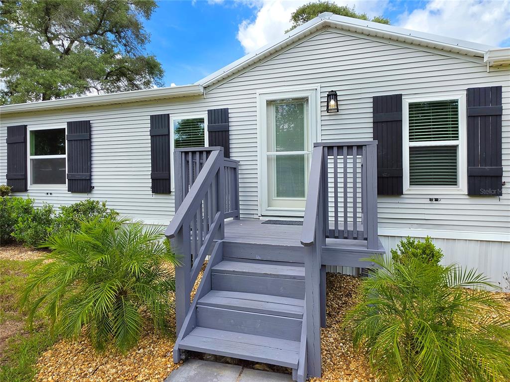 A gray-sided house exterior features a wooden staircase leading to a white front door — 6398 S TROPICANA AVENUE, LECANTO, FL