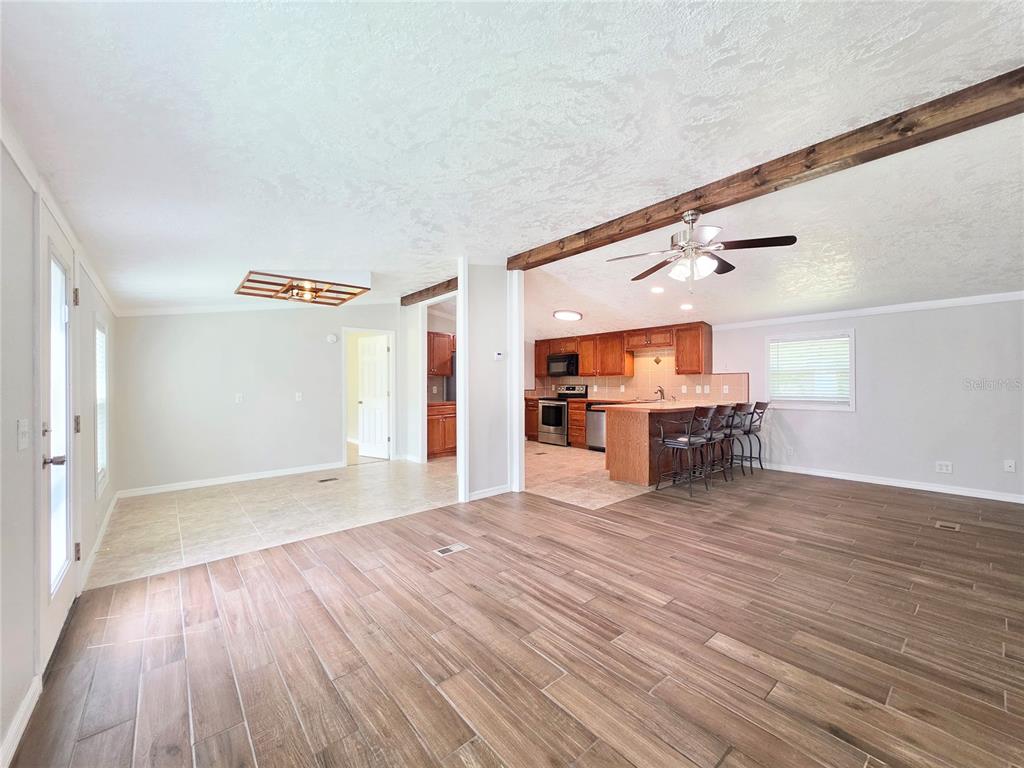 An open-concept living area features wood-look tile flooring, a kitchen island, and exposed ceiling beams — 6398 S TROPICANA AVENUE, LECANTO, FL
