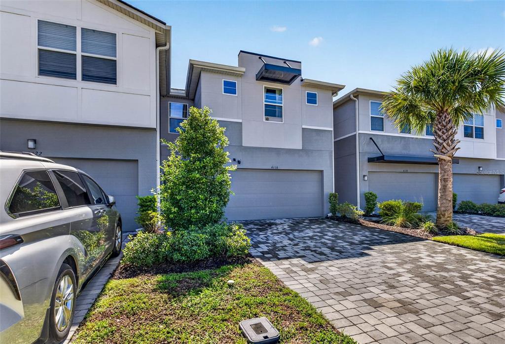 The exterior of a multi-story townhouse complex features paved driveways and a palm tree — 4116 CLOUD HOPPER WAY, LUTZ, FL