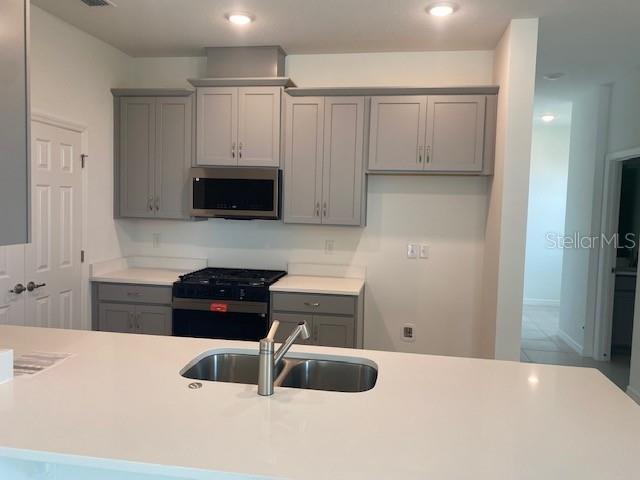 A kitchen features grey cabinets, white countertops, a gas range, and a central island sink — 27329 AFRICAN FISH COURT, HOWEY IN THE HILLS, FL