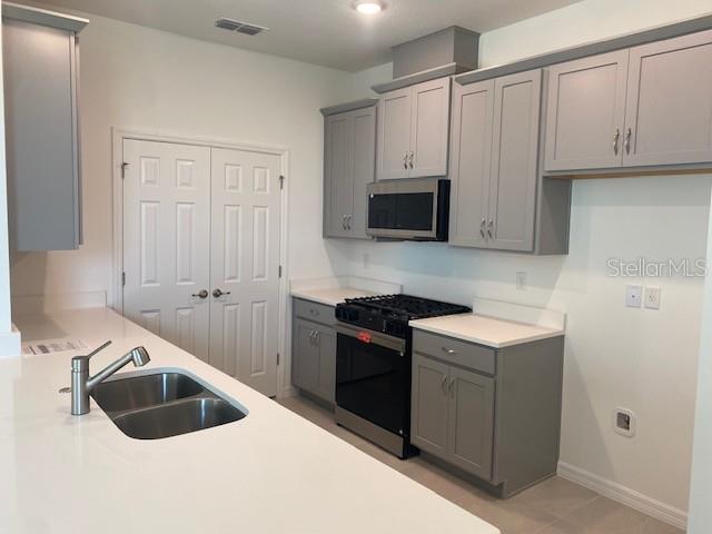 A kitchen features gray cabinets, white countertops, a double sink, and stainless steel appliances — 27329 AFRICAN FISH COURT, HOWEY IN THE HILLS, FL