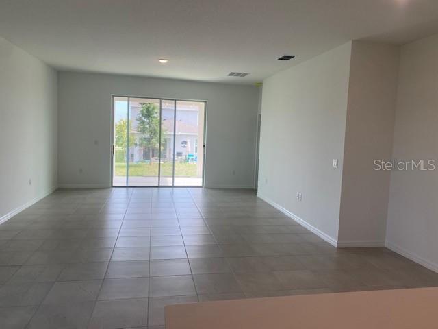 An open-concept room features light-colored tile flooring and a sliding glass door to the backyard — 27329 AFRICAN FISH COURT, HOWEY IN THE HILLS, FL