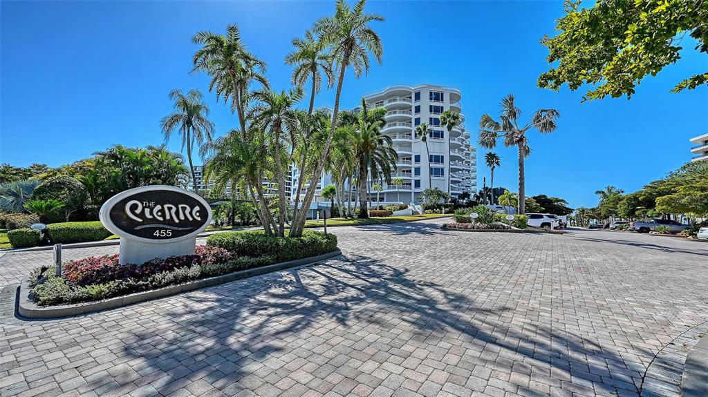A paved driveway leads to a multi-story residential building with palm trees and landscaping — 455 LONGBOAT CLUB ROAD UNIT 905, LONGBOAT KEY, FL