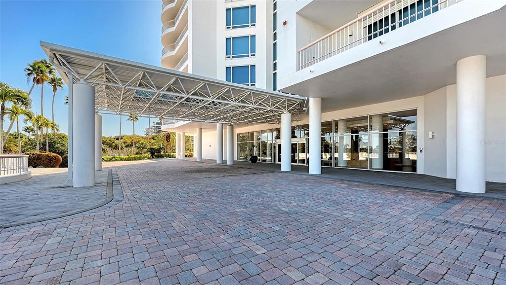A paved driveway leads to the covered entrance of a modern white high-rise building — 455 LONGBOAT CLUB ROAD UNIT 905, LONGBOAT KEY, FL