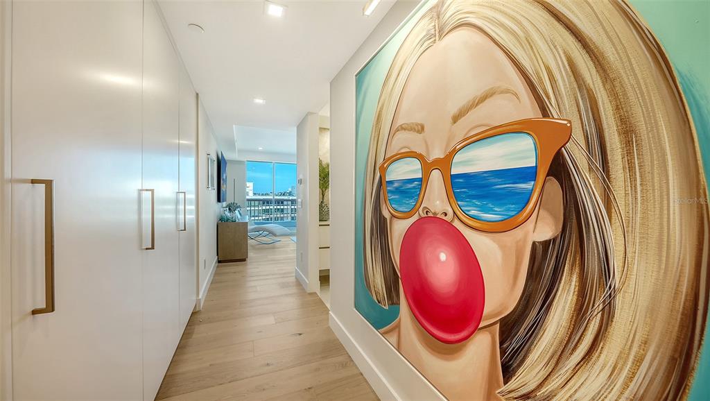 A hallway with light wood floors, white cabinetry, and a large painting of a woman — 455 LONGBOAT CLUB ROAD UNIT 905, LONGBOAT KEY, FL