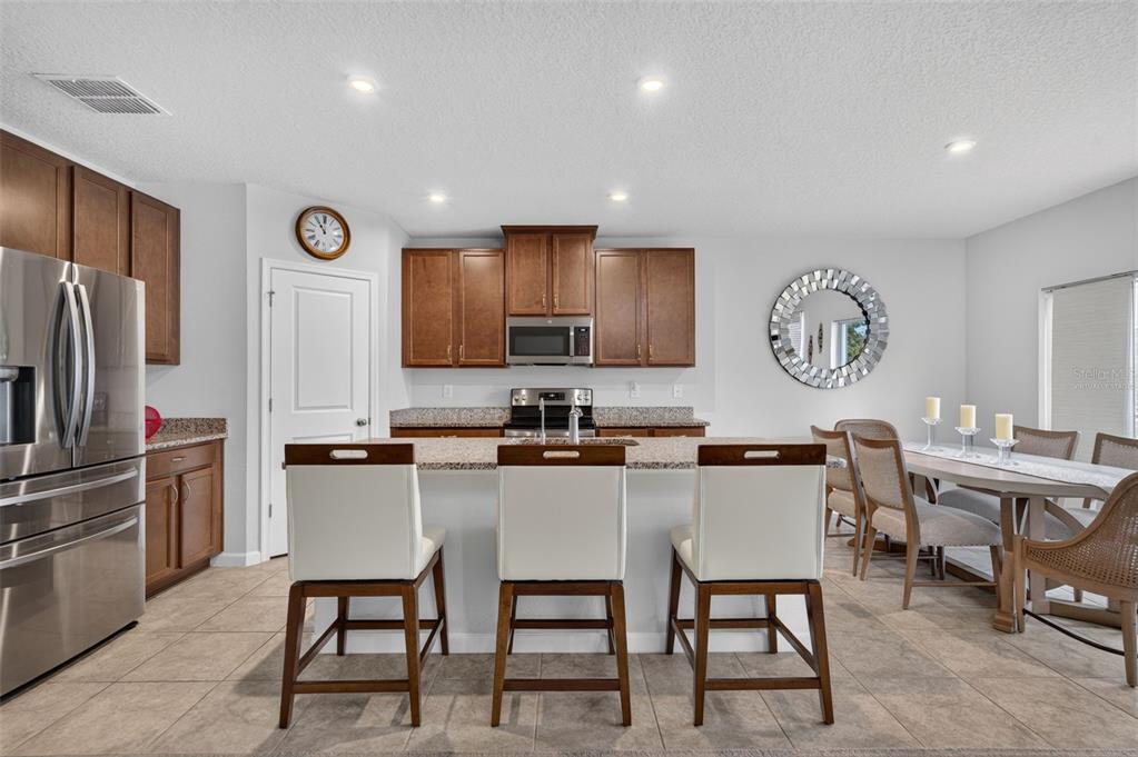 A kitchen with granite countertops and wood cabinets overlooks a dining area and living room — 341 WINTER BLISS LANE, MOUNT DORA, FL