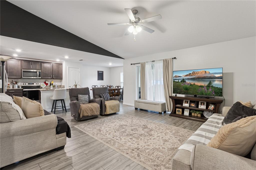 An open-concept living room and kitchen feature gray wood-look flooring and a vaulted ceiling — 1063 LAKE ARBOR COURT, TAVARES, FL