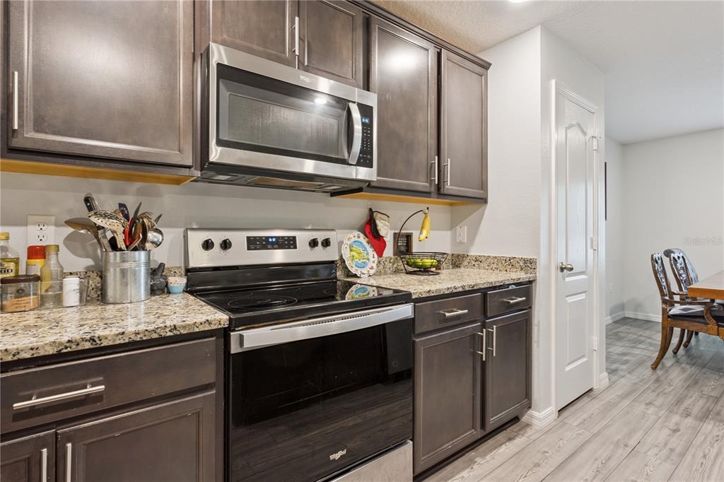 A kitchen features dark wood cabinets, granite countertops, stainless steel appliances, and wood-look flooring — 1063 LAKE ARBOR COURT, TAVARES, FL