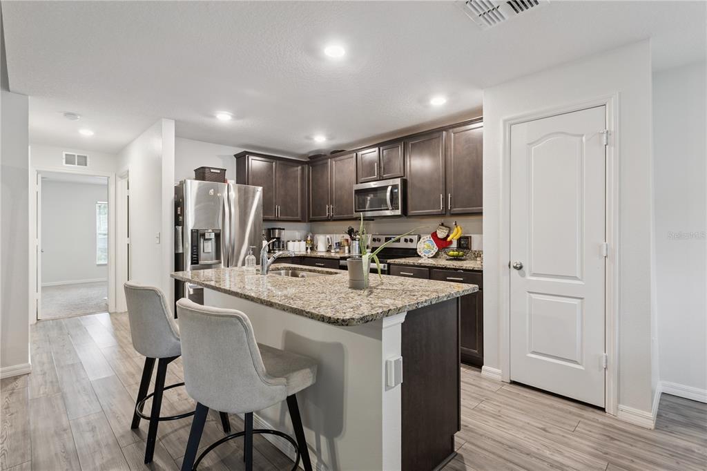 A kitchen features dark wood cabinets, granite countertops, a center island with barstools, and wood-look flooring — 1063 LAKE ARBOR COURT, TAVARES, FL
