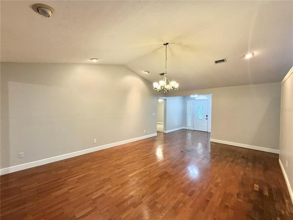 An empty room with hardwood floors, a vaulted ceiling, and a chandelier near the entryway — 11512 NW 13TH LANE, GAINESVILLE, FL