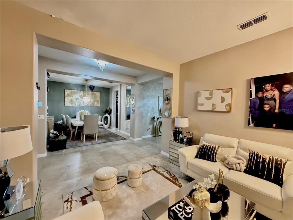 A living room with a white sofa and two ottomans opens into a dining area — 3982 BLOSSOM DEW DRIVE, KISSIMMEE, FL