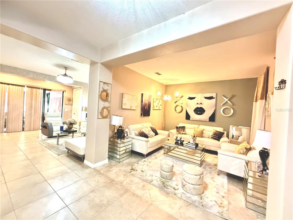 A living room features white sofas, a glass coffee table, and wall art on a beige wall — 3982 BLOSSOM DEW DRIVE, KISSIMMEE, FL