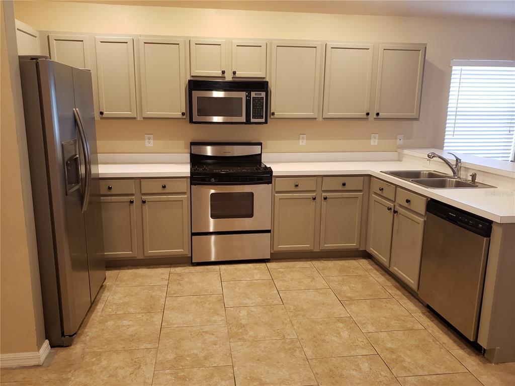 A kitchen features light gray cabinets, stainless steel appliances, white countertops, and tan tile flooring — 31316 TRIBOROUGH DRIVE, WESLEY CHAPEL, FL
