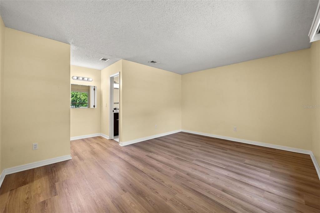 An empty bedroom features light yellow walls, wood-look flooring, and a doorway leading to a bathroom — 2808 TAMARACK TRAIL, APOPKA, FL