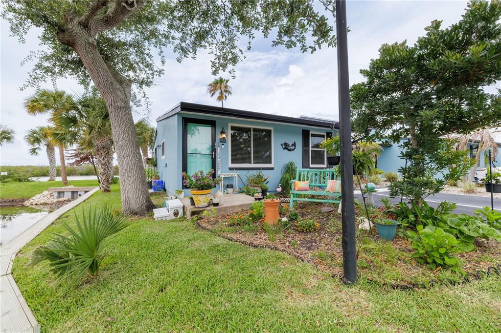 A small, light blue cottage with a front garden, bench, and waterfront view — 100 POINCIANA COVE COURT UNIT 100, NEW SMYRNA BEACH, FL