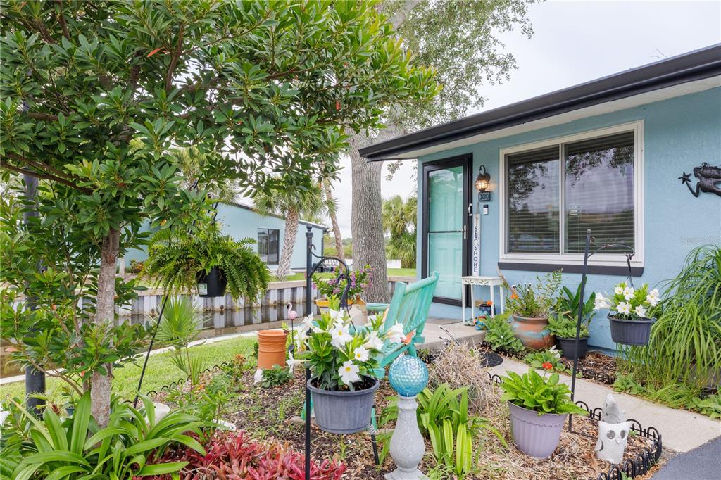 A light blue house exterior features a front porch with potted plants and a chair — 100 POINCIANA COVE COURT UNIT 100, NEW SMYRNA BEACH, FL