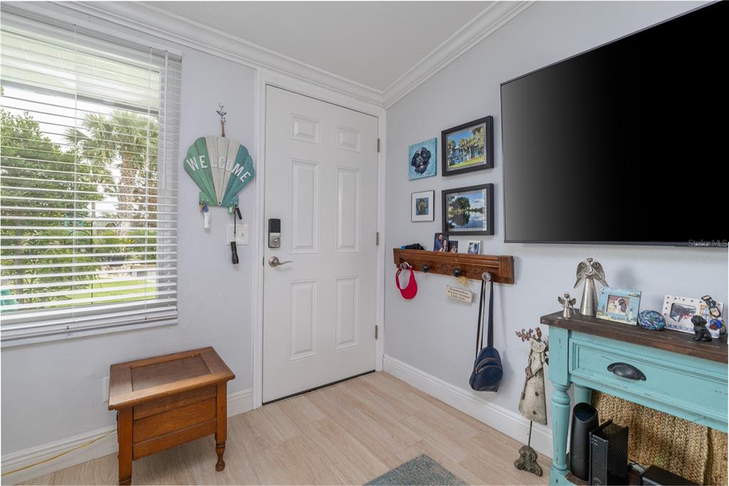 An entryway features a white door, light wood flooring, a television, and a teal console table — 100 POINCIANA COVE COURT UNIT 100, NEW SMYRNA BEACH, FL