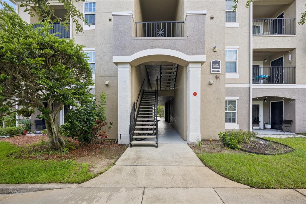 An exterior view of a multi-story apartment building with a central staircase and balconies — 6596 SWISSCO DRIVE UNIT 1512, ORLANDO, FL