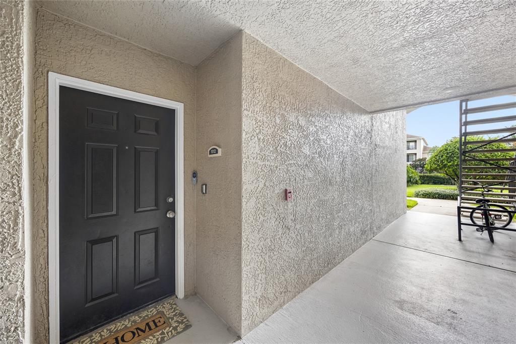 A black front door with a welcome mat sits under a covered exterior walkway — 6596 SWISSCO DRIVE UNIT 1512, ORLANDO, FL